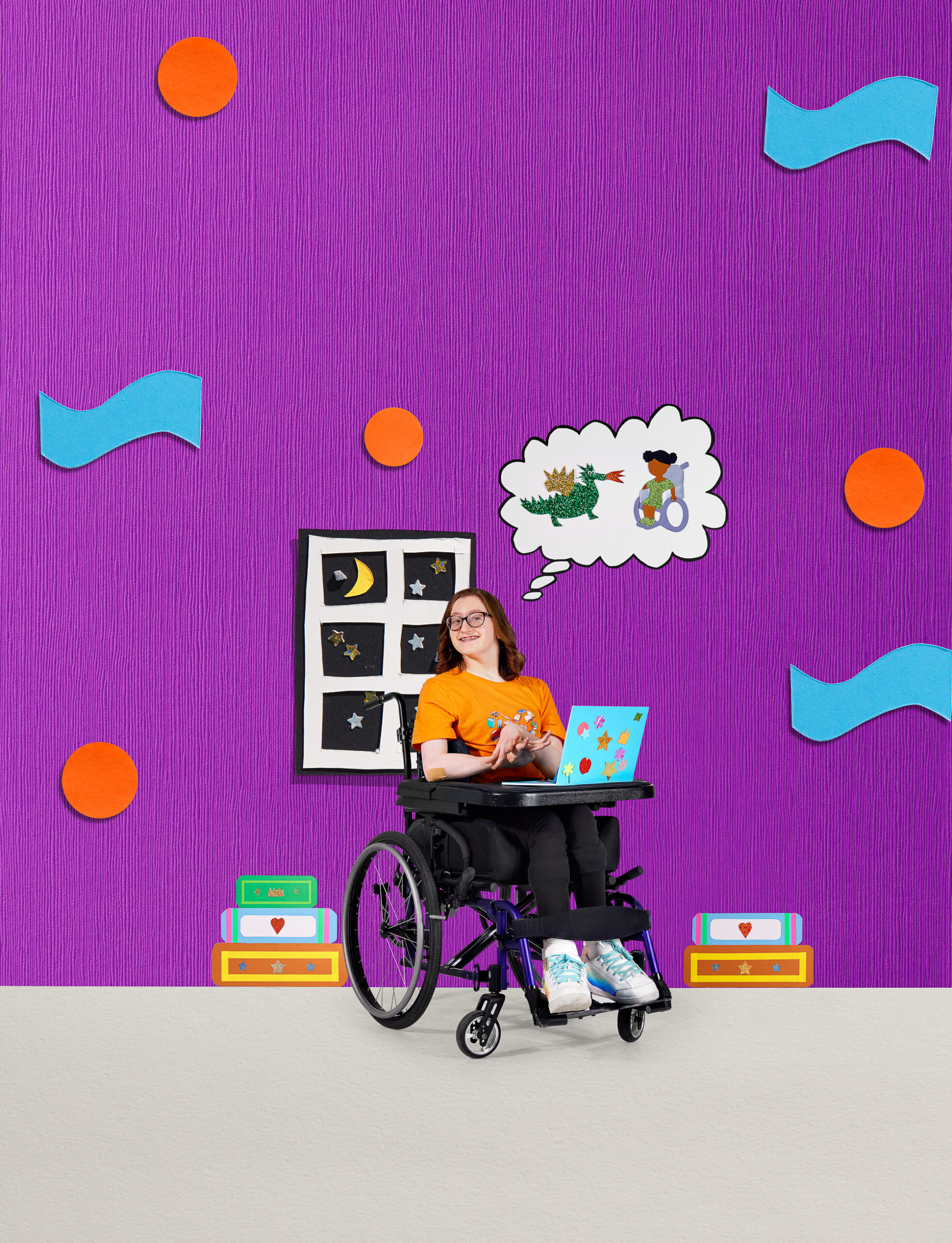 A young person with light skin tone and medium brown hair. She is using a wheelchair and writing on her laptop. A thought bubble appears above her head, featuring a character in a wheelchair and a dragon.