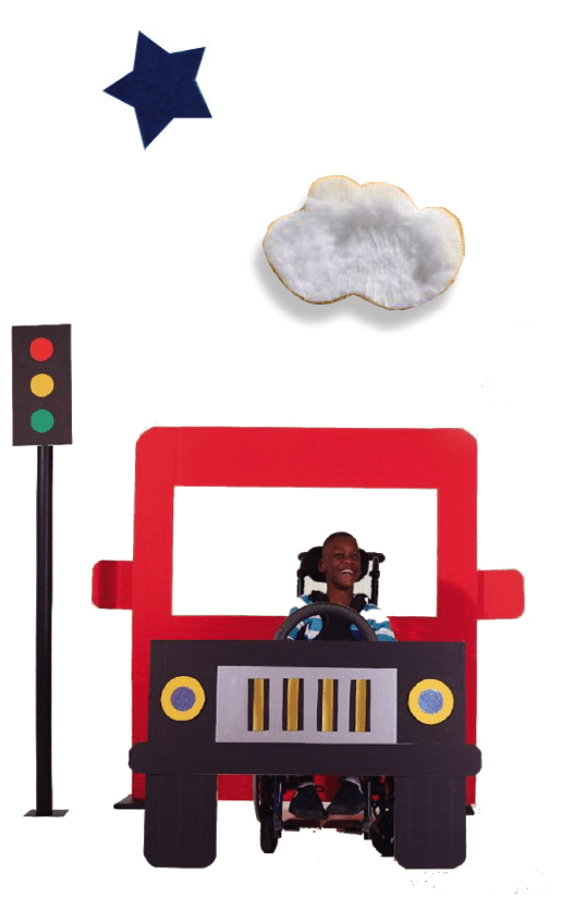 Boy with dark skin tone in a wheelchair, behind the wheel of a red bus.