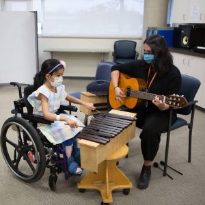 Girl in a wheelchair playing the xylophone with a woman playing the guitar