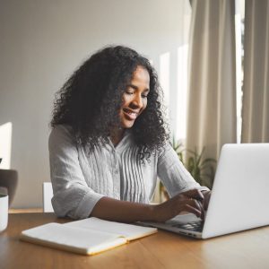 Woman with dark skin and dark hair typing on their laptop
